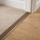 Champagne anodised aluminium door threshold ramp fitted across a doorway where beige twist carpet meets oak-effect laminate on a landing