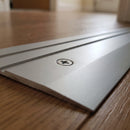 Close-up of the countersunk screw sitting flush in the face of a silver aluminium door threshold ramp, showing the two fine grooves and the feathered edge