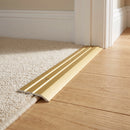 Gold anodised aluminium door threshold ramp fitted across a doorway where cream carpet meets light oak wood flooring in a traditional home