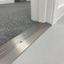Inox anodised aluminium door threshold ramp fitted across a doorway where grey contract carpet tile meets pale grey safety vinyl in an office