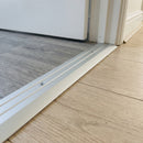 Silver anodised aluminium door threshold ramp fitted across a doorway where grey wood-effect LVT meets pale oak laminate in a modern home