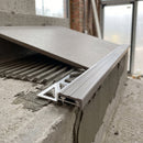Close-up of the tile-in stair nosing during installation, perforated aluminium leg bedded in tile adhesive with the tread tile being laid over it