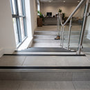 Aluminium tile-in stair nosing with black anti-slip insert fitted to every tread of a grey porcelain tiled commercial staircase in a UK office reception