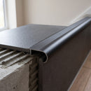 Black tile-in aluminium stair nosing bedded into adhesive at the edge of an anthracite porcelain tiled step