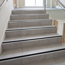Tile-in stair nosing with Black anti-slip insert on a light grey porcelain tiled office staircase, silver aluminium body and riser apron on each tread