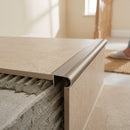 Champagne tile-in aluminium stair nosing bedded into adhesive at the edge of a beige porcelain tiled step
