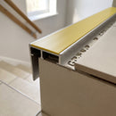 Close-up of a tile-in stair nosing showing the perforated leg bedded under the tread tile, the tile finishing flush to the profile and the apron covering the riser edge