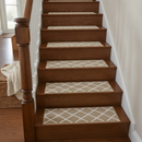 Beige diamond-pattern non-slip carpet stair tread pads fitted to a dark oak staircase beside a wicker basket and knitted throw