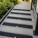 Stainless steel treadplates with black grit centres screwed along grey composite decking steps beside green shrubs