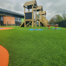 Green artificial playground safety turf beneath a wooden climbing frame with orange rubber safety surfacing border