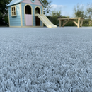 Light grey artificial playground safety turf in a soft play garden with a pastel playhouse and wooden bench