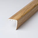 uPVC wood effect stair nosing in Oak on a plain studio background, 30mm x 30mm angle profile with fixing channels visible at the cut end