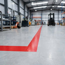 Red vinyl line marking tape marking a hazard zone boundary on a warehouse floor with forklift in background