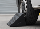 Rubber wheel chock wedged against the rear tyre of a van in a warehouse loading bay yard