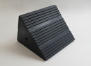 Black solid rubber heavy duty wheel chock on a neutral studio background, showing the ribbed grip tread and rope hole