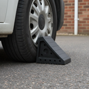 Rubber wheel chock wedged against the rear tyre of a white van on a driveway