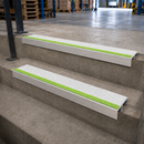 Two aluminium stair nosings with white and green anti-slip inserts fitted to concrete warehouse steps
