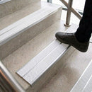 Foot stepping onto pale concrete stairs fitted with twin white anti-slip inserts in aluminium nosings