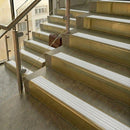 Brass stair nosings with white ribbed inserts on stone steps beside a glass balustrade