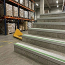 White and green insert stair nosings fitted along wide concrete warehouse steps beside racking and a pallet truck