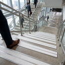 White twin-insert stair nosings on a glazed office stairwell, with people descending the flight beyond