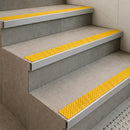 Tile-in stair nosings with yellow anti-slip inserts set flush into grey tiled steps beside tactile paving