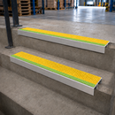 Two aluminium stair nosings with yellow and green anti-slip inserts fitted to concrete warehouse steps
