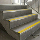 Aluminium tile-in stair nosing with a high-visibility yellow anti-slip PVC insert on a grey tiled staircase