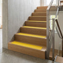 Bright yellow inserts on oak timber stairs indoors, viewed alongside a steel and glass balustrade