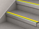 Yellow and green insert stair nosings fitted to two pale grey steps against a white stringer wall